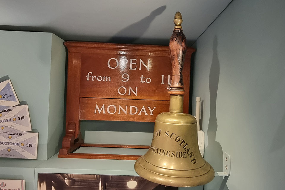 Branch opening hours sign and large brass bell